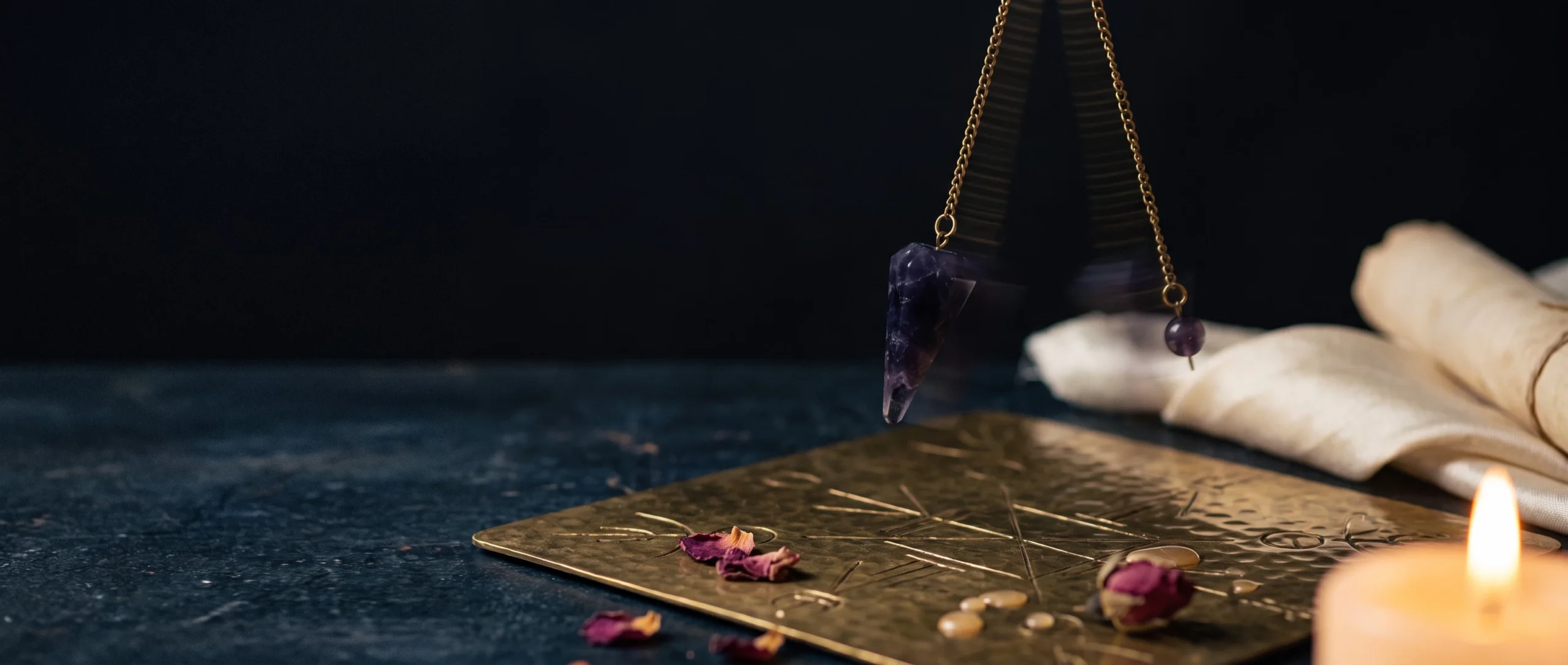 A crystal pendulum on a brass chain caught mid-swing over a brass divination board on a dark surface.