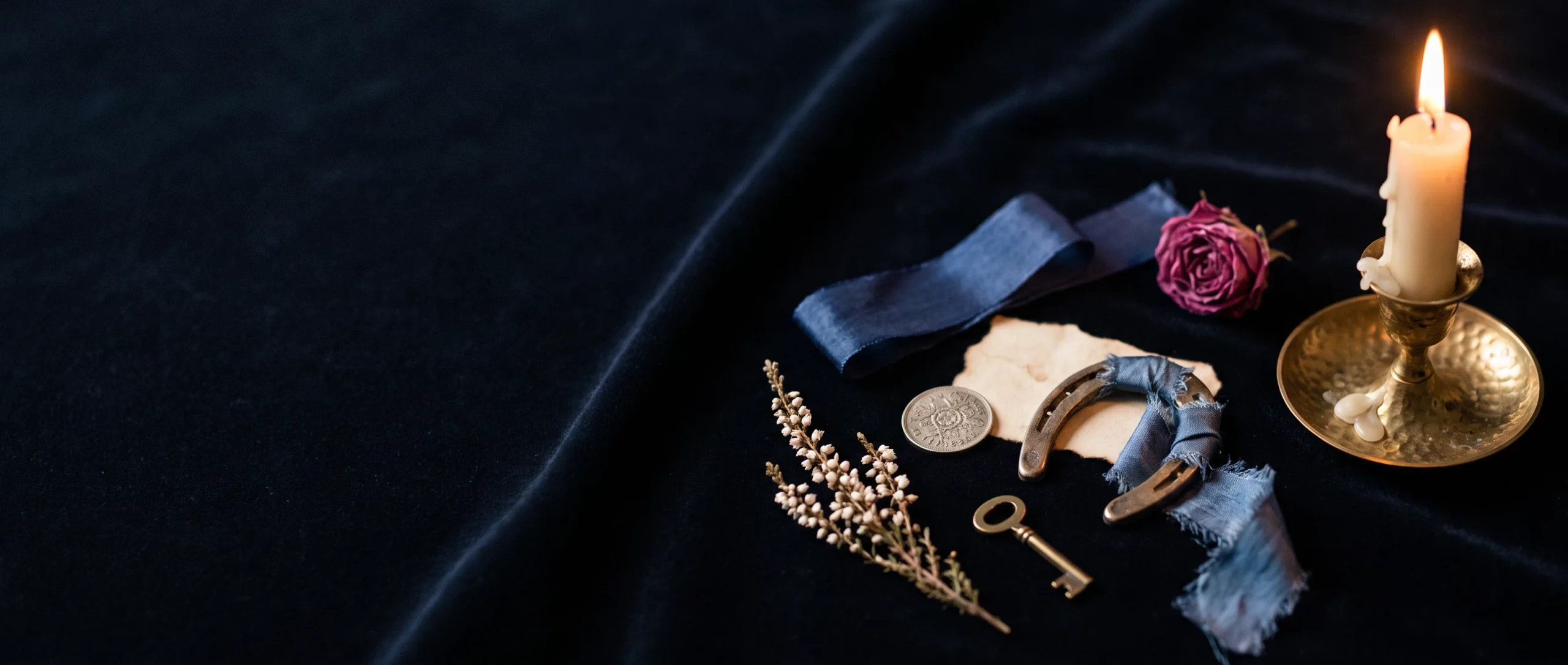 Wedding luck charms — a horseshoe, a sixpence, a key, white heather, and blue ribbon — on dark velvet.