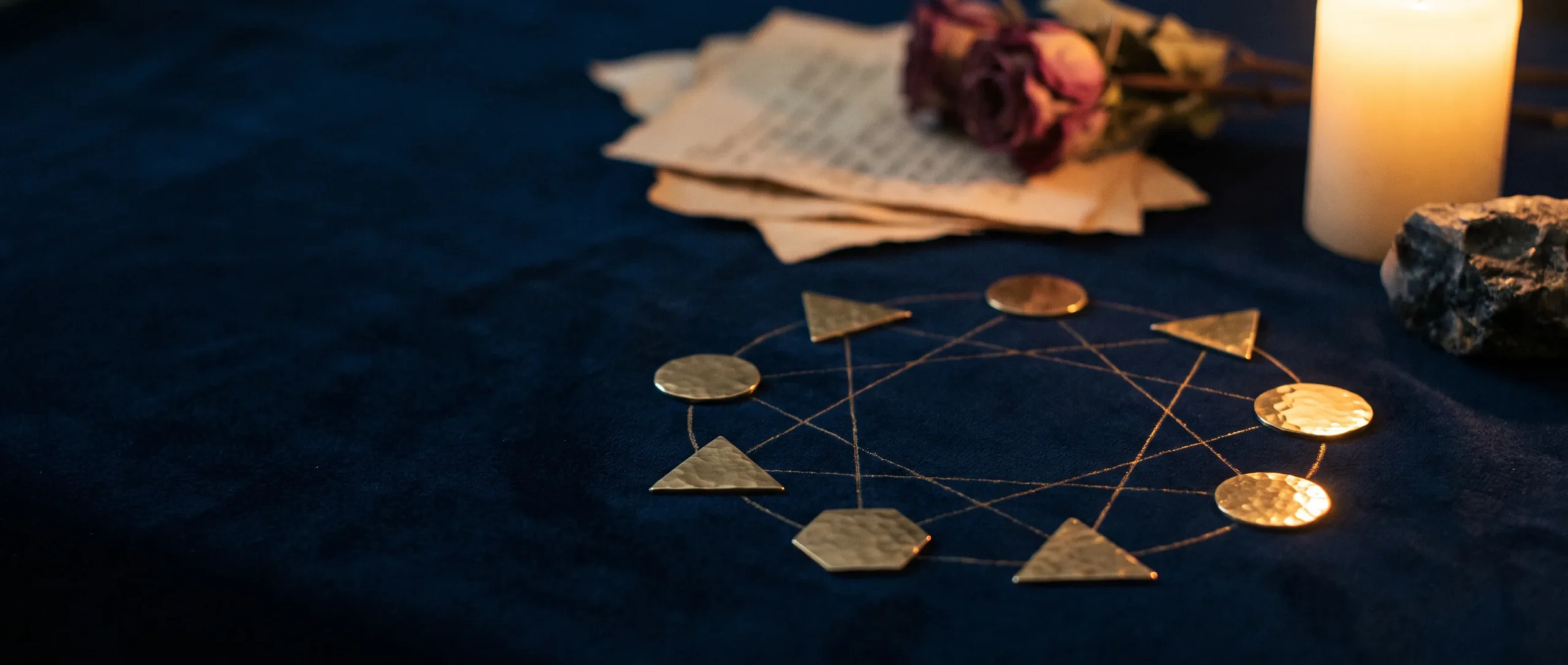 Nine brass geometric tokens arranged around an etched gold circle with connecting lines, on dark velvet by candlelight.