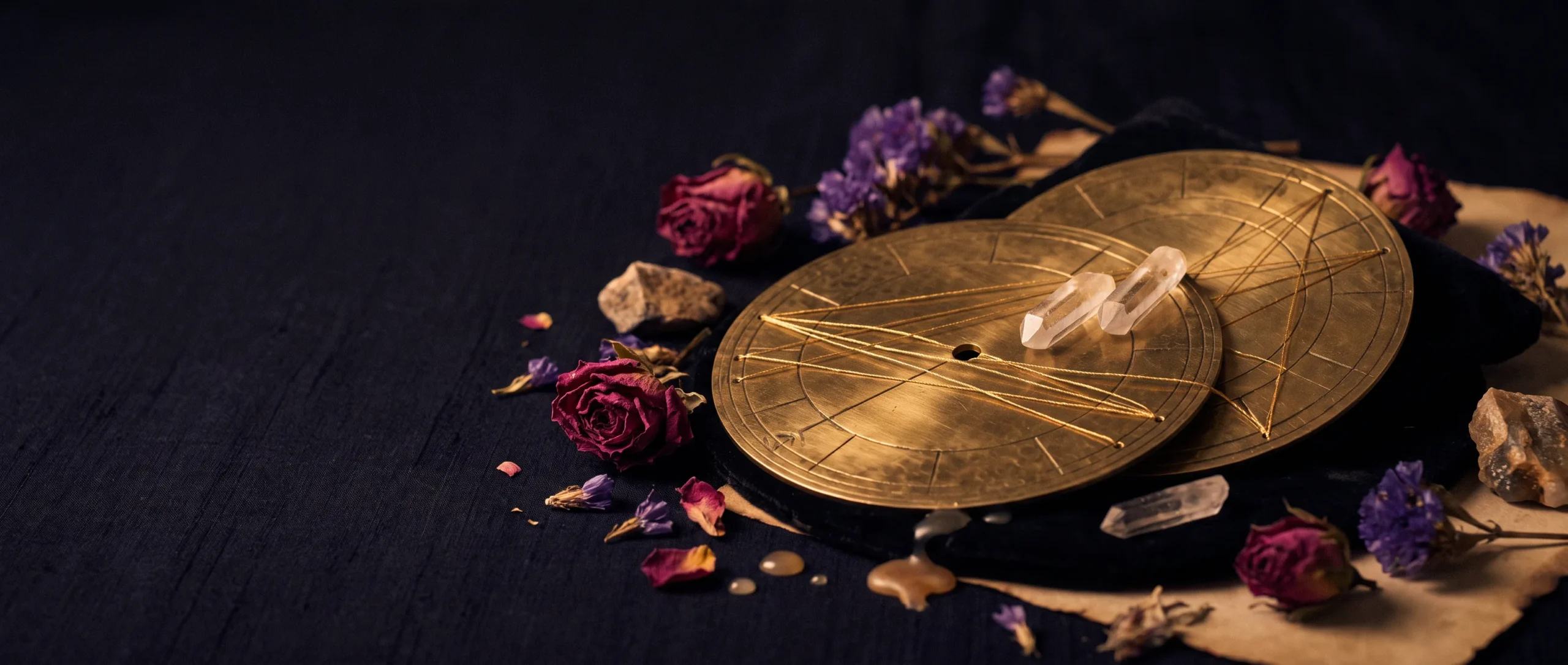- Two engraved brass astrology-wheel discs overlapping on dark velvet, joined by fine gold aspect lines, with crystal points where they meet.